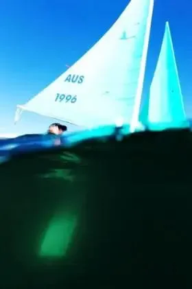 水面すれすれから見上げた白いセールのハンザ。水中と水上が半分ずつ写っている